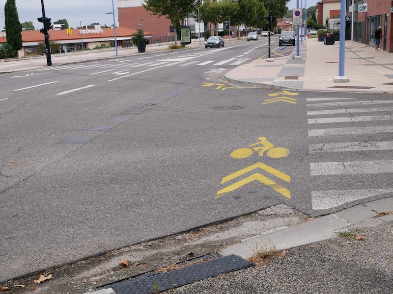 Vue sur le carrefour avec des pictos vélo en jaune qui partent du trottoir
